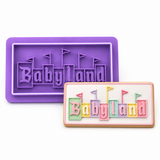 'Babyland' embossed in the center, shown next to a decorated rectangular cake or cookie with pastel-colored letters spelling 'Babyland' on a white background.