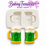 Baking Treasures Bake Shop St. Patrick's Day shamrock beer mug silicone mold on a white background with two green and gold decorated beer mugs, white frothy tops, and lavender bow branding.