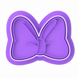 Stick Bow cookie cutter and embosser two-piece set with decorated bow sugar cookie on a white background.