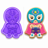 Royal Orchid Lavender luchadora cookie cutter and embosser shown beside a decorated sugar cookie featuring a cute masked wrestler with a turquoise mask, pink cape, purple shorts, heart belt, and colorful icing details on a white background.