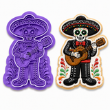 Royal Orchid Lavender Día de los Muertos Skeleton Mariachi Guitar Cookie Cutter & Embosser shown beside a decorated sugar cookie featuring a festive sugar skull mariachi wearing a sombrero and playing a guitar on a white background.